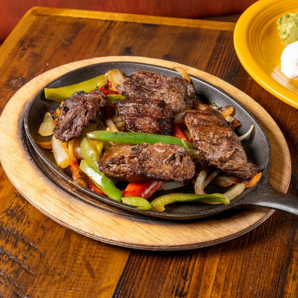 Sizzling Frida's Mexican Grill fajitas with steak, onions, and bell peppers in a cast iron skillet.