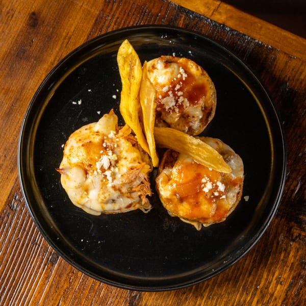 Three cheesy baked potatoes with sauce and crumbled cheese, garnished with plantain chips on a black plate.