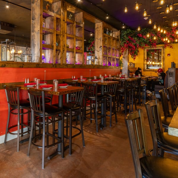 Restaurant interior with high-top tables, red walls, wooden shelves, and hanging lights with red floral decor.