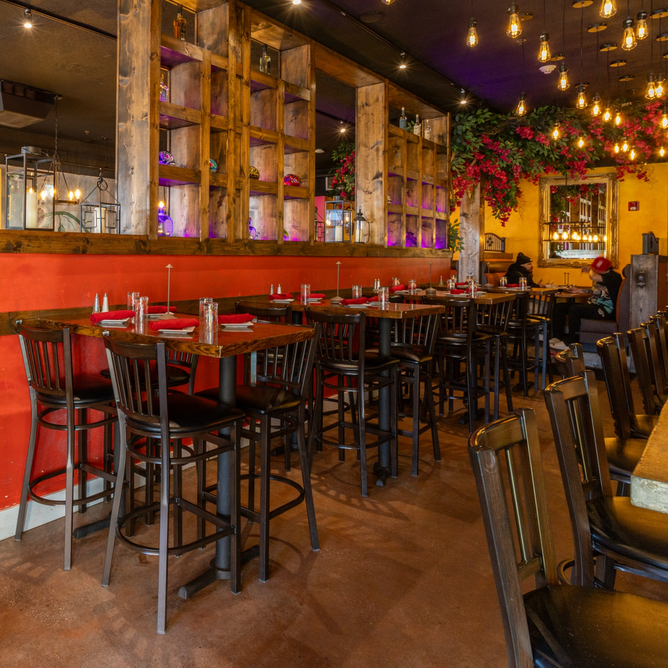 Restaurant interior with high-top tables, red walls, wooden shelves, and hanging lights with red floral decor.