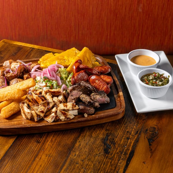 Frida's Mexican Grill's mixed grill platter with various meats, plantains, and sauces on a wooden board.