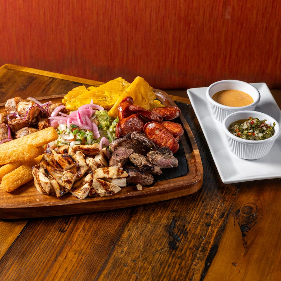 Frida's Mexican Grill's mixed grill platter with various meats, plantains, and sauces on a wooden board.