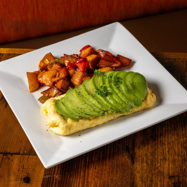 Frida's Mexican Grill omelet topped with sliced avocado and parsley, served with seasoned potatoes.