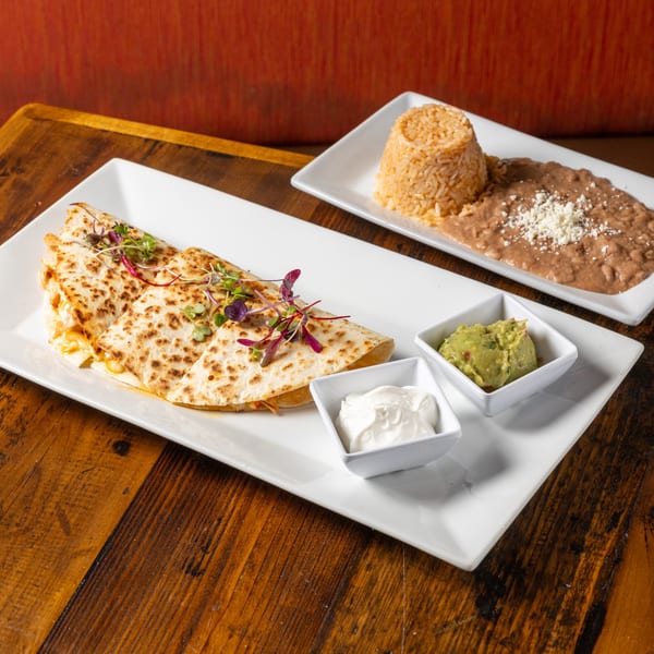 Frida's Mexican Grill quesadilla with guacamole, sour cream, rice, and refried beans on a wooden table.