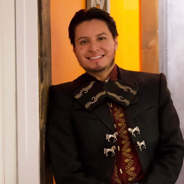 Smiling man in a black charro suit with silver horse buttons and a patterned red shirt.