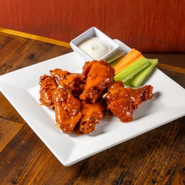 Frida's Mexican Grill's spicy chicken wings with ranch, carrots, and celery on a white plate.
