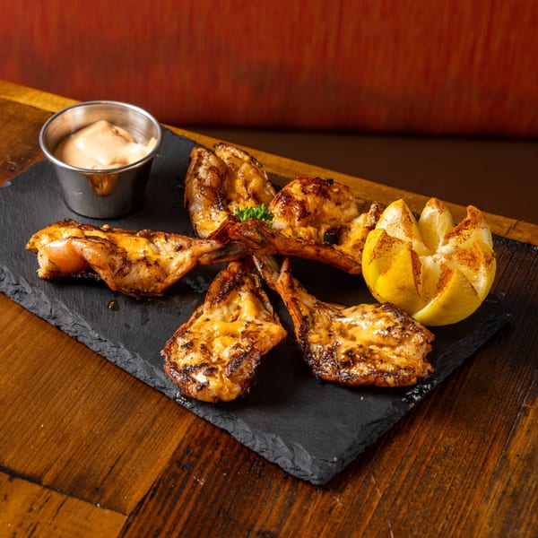 Grilled shrimp with sauce and a carved lemon on a dark slate board at Frida's Mexican Grill.