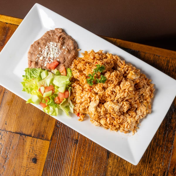 Chicken and rice with refried beans and a side salad on a white rectangular plate.