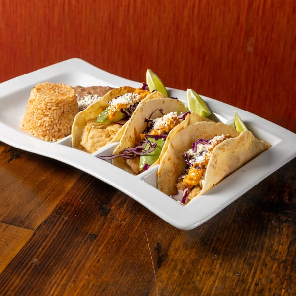 Three Frida's Mexican Grill tacos with rice and beans, garnished with lime, on a white plate.