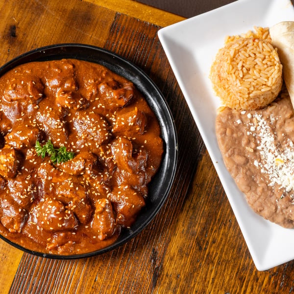 Frida's Mexican Grill's chicken mole with rice, refried beans, and tortillas on a wooden table.