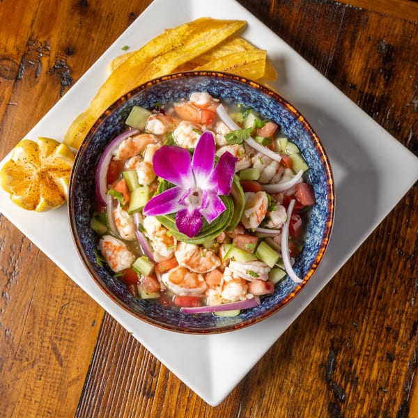 Shrimp ceviche in a blue bowl, garnished with a purple orchid, avocado, and plantain chips.