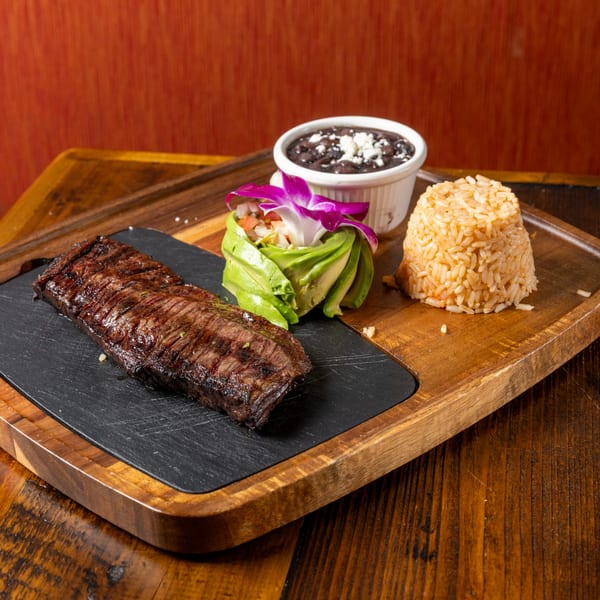 Grilled steak, rice, black beans, and avocado salad with a purple orchid on a wooden board.
