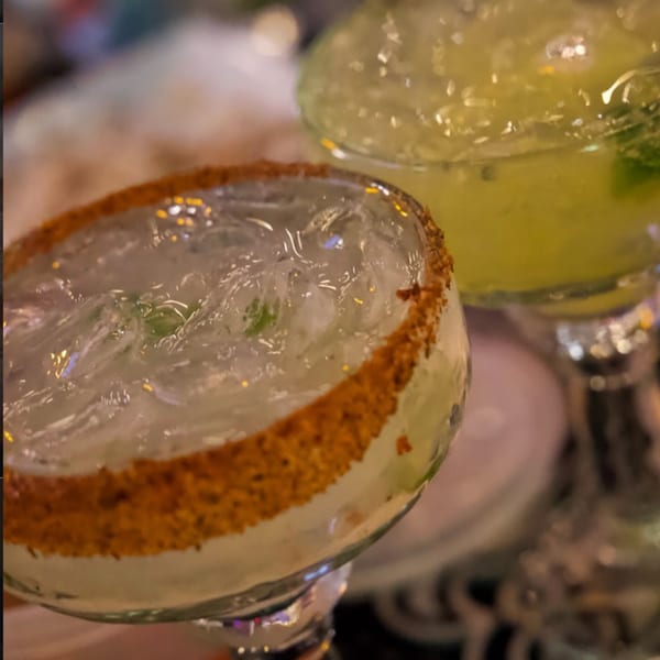 Two margaritas, one with a chili-salted rim, filled with ice and lime, on a dark background.