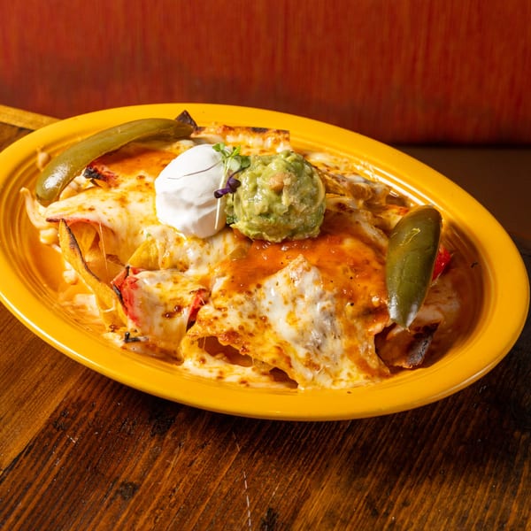 Frida's Mexican Grill's cheesy nachos with guacamole, sour cream, and jalapeños on a yellow plate.