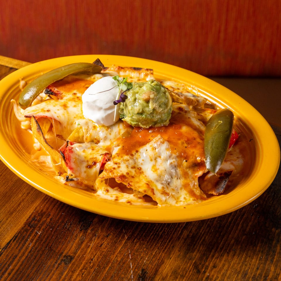 Frida's Mexican Grill's cheesy nachos with guacamole, sour cream, and jalapeños on a yellow plate.
