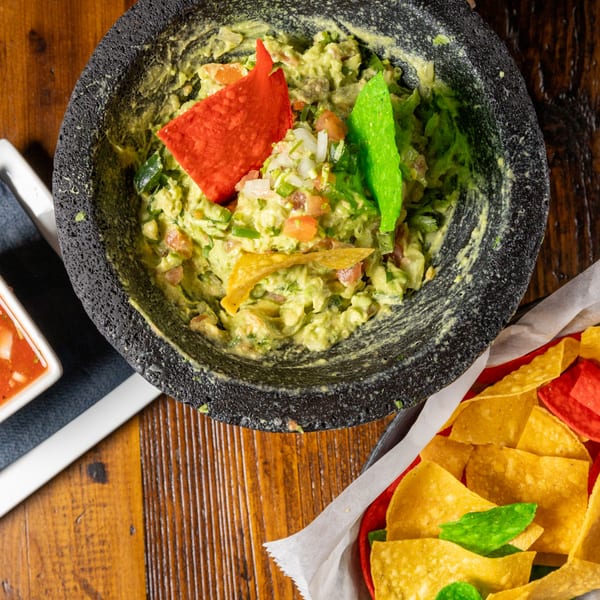 Guacamole in a stone bowl with colorful tortilla chips, alongside a basket of chips and salsa.