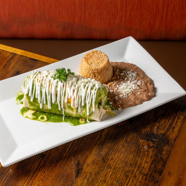 A Frida's Mexican Grill burrito covered in green sauce, sour cream, and cheese, with rice and beans.
