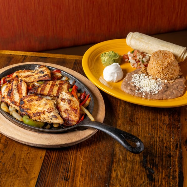 Frida's Mexican Grill chicken fajitas with grilled peppers and onions, served with rice, beans, and tortillas.