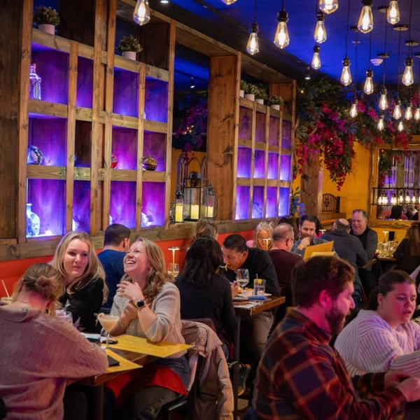 Diners enjoying a lively evening in a restaurant with purple-lit shelves and hanging Edison bulbs.