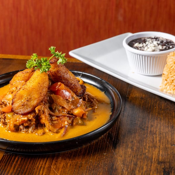 Frida's Mexican Grill's Ropa Vieja with plantains, rice, and black beans on a wooden table.