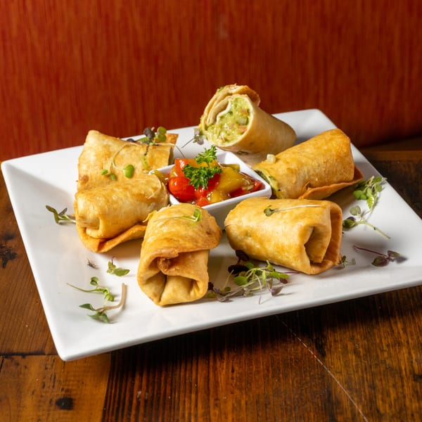Frida's Mexican Grill's golden-fried flautas with guacamole and salsa on a white rectangular plate.