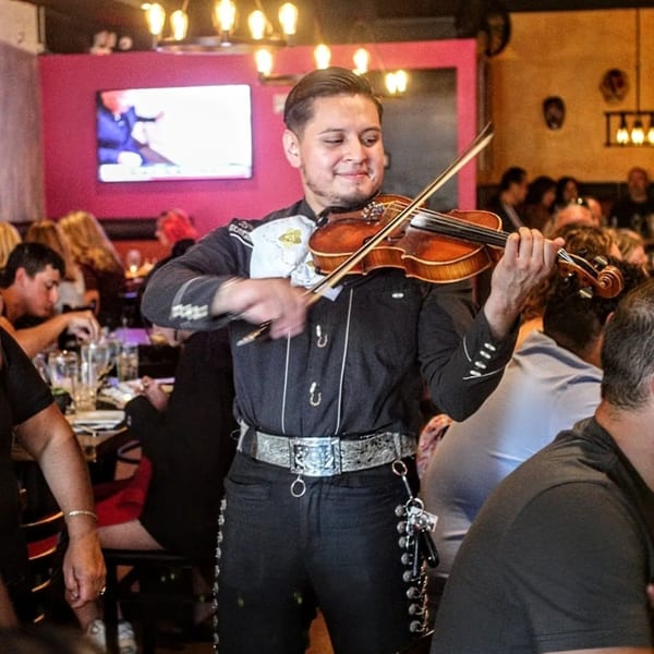 A mariachi musician in traditional attire plays the violin for restaurant patrons.