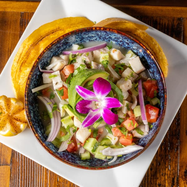 Ceviche with avocado, red onion, tomatoes, and a purple orchid, served with plantain chips and lemon.