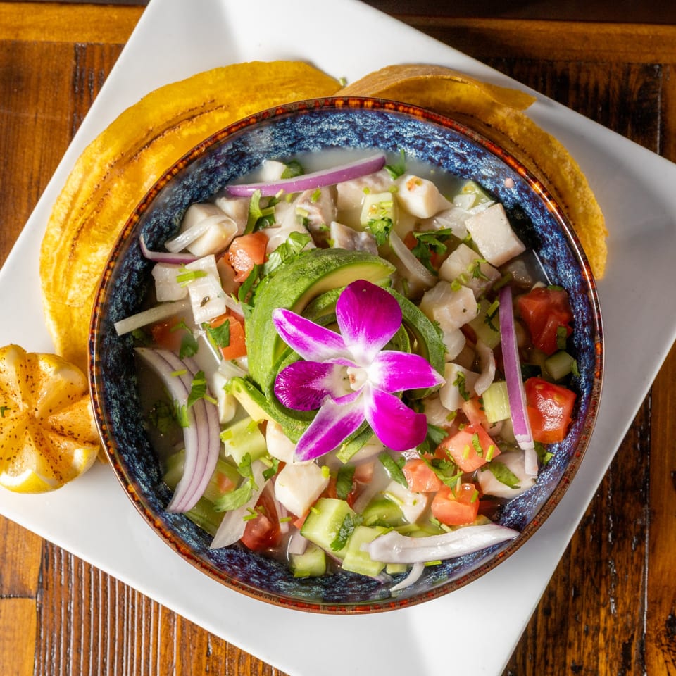 Ceviche with avocado, red onion, tomatoes, and a purple orchid, served with plantain chips and lemon.