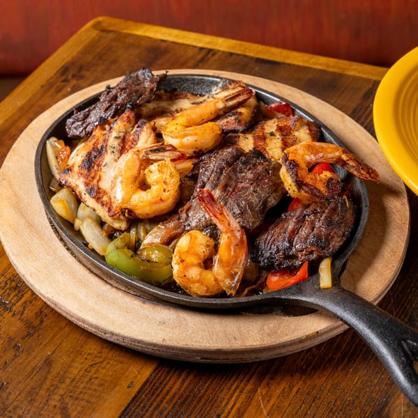 Sizzling fajitas with grilled shrimp, chicken, steak, onions, and bell peppers in a cast iron skillet.