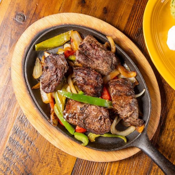 Sizzling beef fajitas with grilled onions and bell peppers in a cast iron skillet on a wooden table.