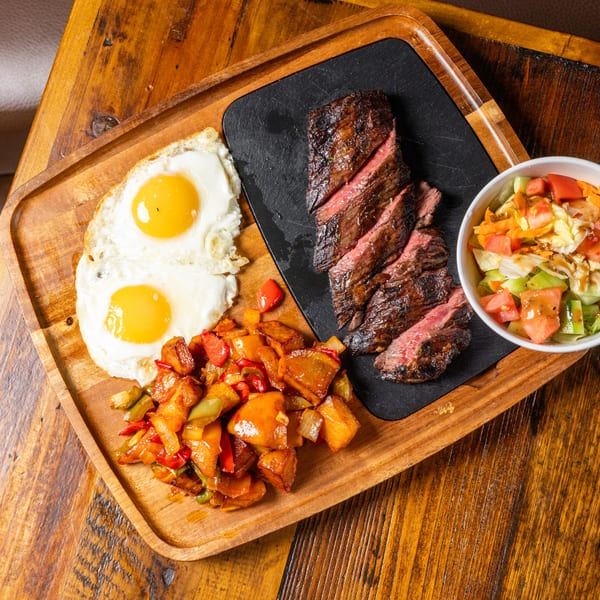 Steak and eggs breakfast with home fries and a side salad on a wooden tray.